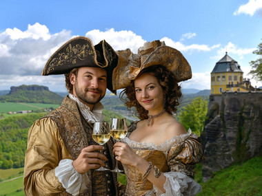 Barock gekleidetes Paar mit Weingläsern vor der Friedrichsburg