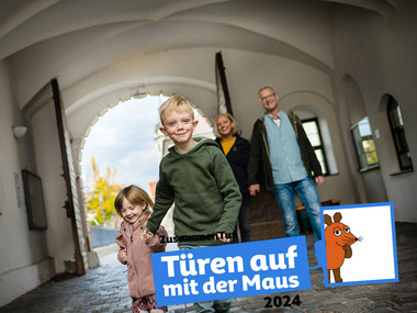 Zwei Kinder, ein Junge und ein Mädchen, rennen durch das mächtige Portal in den Schlosshof.