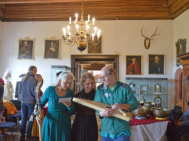 Mitwirkende Kpnstler des Campa Festivals stehen im historischen Saal und präsentieren ihre selbst gebauten Instrumente