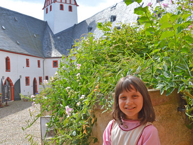 Mädchen als Burgfräulein verkleidet, im Hintergrund Burghof von Schloss Rochsburg mit Pulverturm