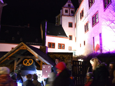 Bunt angestrahlte Fassade der Rochsburg, im Vordergrund Gästeführer Michael Kreskowsky am Backofen mit einer Gästegruppe