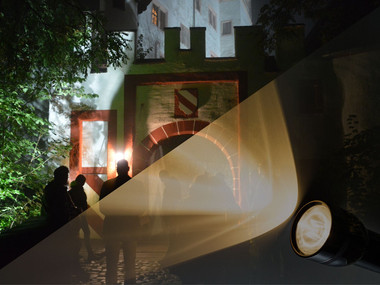 Abendaufnahme, das vordere Burgtor bei Nacht, Umrisse von Menschen, die vor dem Burtor warten, eine Taschenlampe scheint ins Bild
