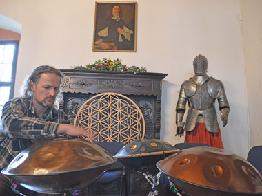 Thomas Plum, einer der Mitorganisatoren des Campana Festivals, spielt auf einem Handpan, im Hintergrund eine historische Kommode, ein Schönburgisches Porträt sowie eine alte Ritterrüstung